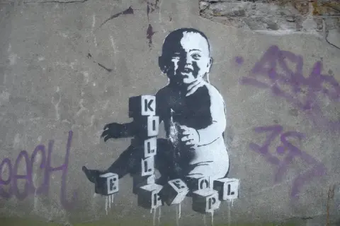 Dziecko bawi się klockami z literami, tworząc napis "KILL". To mocne co to jest graffiti, które prowokuje do myślenia.