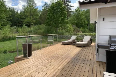 Ny slipad trall på altanen med solstolar och grill, redo för sommarens njutning i grönskan.
