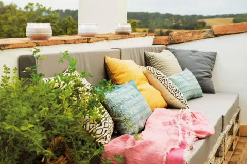 Sofá de palets con cojines coloridos y manta rosa, perfecto para una decoración chill out interiores. Velas aromáticas en la barandilla.