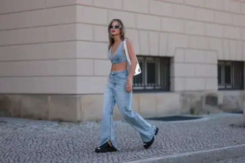 Modna kobieta w jeansach bootcut i denimowym topie, z białym przezroczystym plecakiem. Stylowe jeansy bootcut stylizacje.
