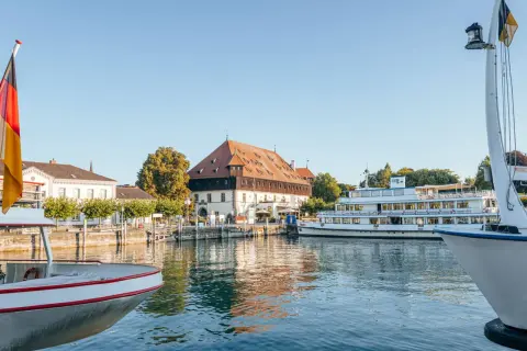 Boote am Bodensee, deutsche Flagge weht. Ein historisches Gebäude und ein Ausflugsschiff laden zu Konstanz Events ein.