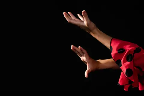 Manos expresivas de una bailaora de flamenco español, con un vestido rojo de lunares negros.