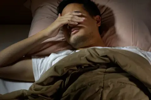 Man in bed, hand over eyes, can't sleep after long run. The runner's mind races, body tired but brain won't switch off.