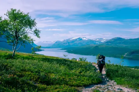 Vandra i Norrland med storslagen utsikt över sjö och snöklädda berg. En ensam vandrare med ryggsäck går på en stenstig.