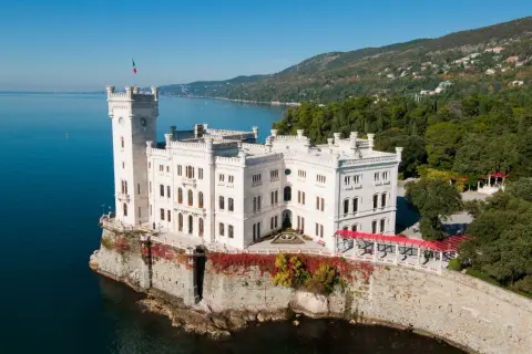 Vitt slott vid havet i Trieste, Italien, med en italiensk flagga på tornet.