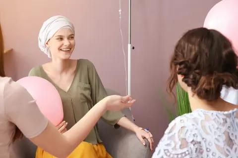 Freundinnen geben einer Frau mit Krebs während der Chemotherapie aufmunternde Worte und halten Ballons.