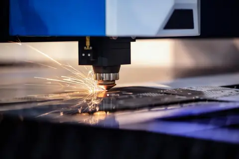 Precyzyjne cięcie aluminium przez laser, iskry rozbłyskują podczas pracy maszyny.
