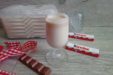 Pyszny likier z kinder czekoladek w kieliszku, obok batoniki i kawałek czekolady.