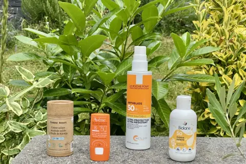 Quatre produits solaires, dont une crème solaire sans octocrylene, sont présentés sur un muret, entourés de verdure.