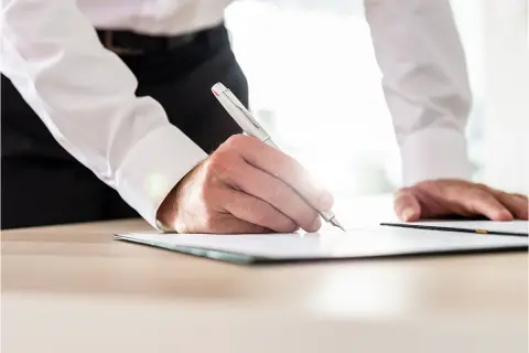 Mężczyzna w białej koszuli podpisuje dokument. Dowiedz się, jak sprawdzić, kto jest właścicielem mieszkania w bloku.