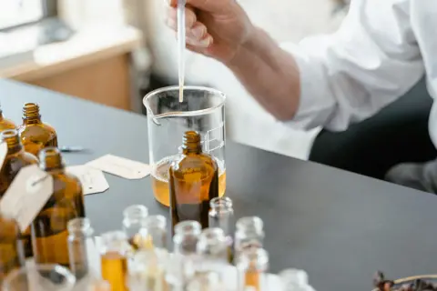 Ricerca su coumarin cos'è: un profumiere testa essenze in ambrate bottigliette, con un contagocce in un becher.