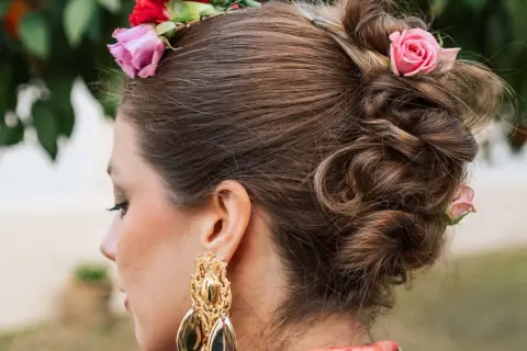 Peinado recogido con flores, estilo flor flamenca pelo suelto, luciendo un gran pendiente dorado.