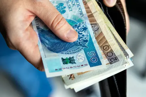 Dłoń trzyma polskie banknoty 50 i 200 zł. Zastanawiasz się nad nowymi zasadami przejścia na emeryturę? Tabela z wyliczeniami pomoże Ci to zrozumieć.