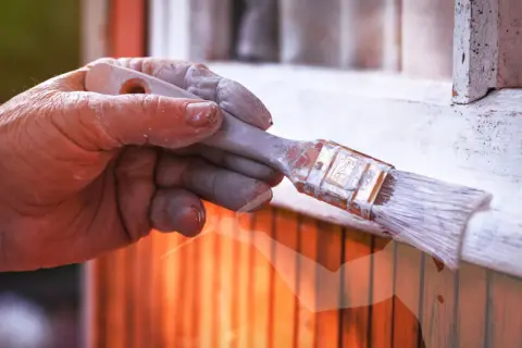 Main d'un peintre avec de la peinture blanche sur les doigts, tenant un pinceau. Astuces pour savoir comment enlever de la peinture sur les mains après le bricolage.
