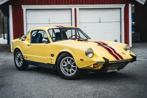 Gul Saab Sonett 2 med röda ränder, parkerad framför ett rött garage.