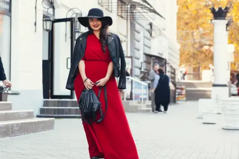 Kobieta w czerwonej sukni i czarnej ramonesce prezentuje stylowe stylizacje dla grubych nóg. Czarny kapelusz dodaje elegancji.