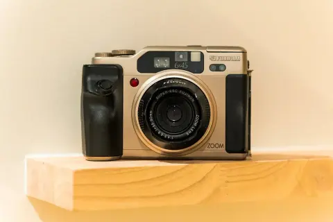 A gold Fujifilm 645 camera with a black grip sits on a wooden shelf.