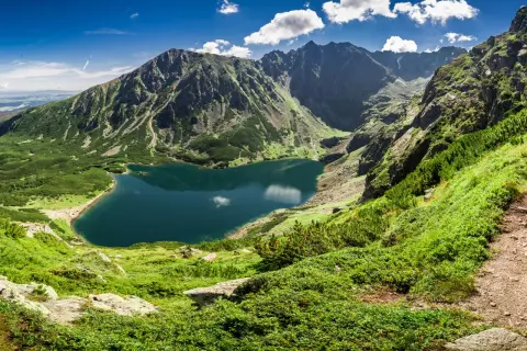 Bergsee in Polen, umgeben von grünen Hängen und schroffen Gipfeln. Die beste Reisezeit für solche Ausblicke ist der Sommer.