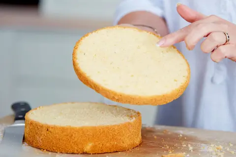 Perfekter tortenboden rezept: Eine Hand hebt eine goldbraune Kuchenschicht über eine zweite, die auf einem Holzbrett liegt.