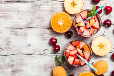 Sangria ricetta bar: bicchieri pieni di frutta fresca, arancia, mele, ciliegie e albicocche su un tavolo di legno.