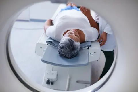 Une femme âgée se repose sur une table d'examen, prête pour un examen PET scan. C'est quoi un PET scan ? Une technique d'imagerie médicale.