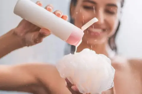 Mujer sonriente aplica shower cream para que sirve: limpieza e hidratación para una piel suave y radiante.