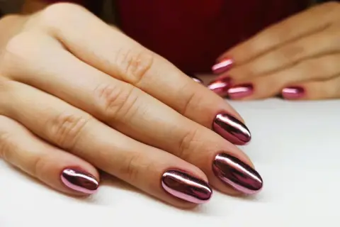 Dłonie z błyszczącym, metalicznym różowym manicure tytanowym. Czy ten efektowny manicure tytanowy rakotwórczy jest wart ryzyka?