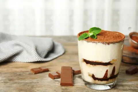 Szybki deser z niczego: kremowe tiramisu w szklance, posypane kakao i udekorowane miętą. Obok kawałki czekolady.