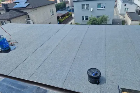 Nowy dach z papy na styropianie, gotowy na ochronę domu. Widać butlę gazową i wiadro z materiałami.