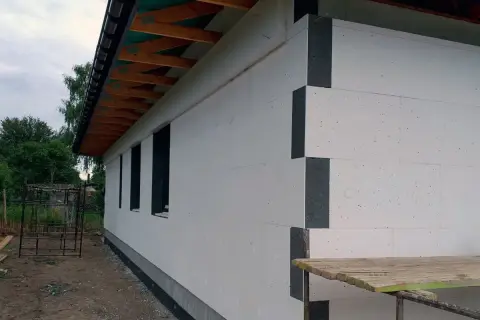 Budowa domu z białego styropianu, który jest świetnym izolatorem. Widać drewniane elementy dachu i okna.