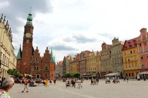 Buntes Treiben auf dem Marktplatz der Breslau Innenstadt. Das Rathaus mit seinem markanten Turm dominiert die Szene, umgeben von farbenfrohen Bürgerhäusern.