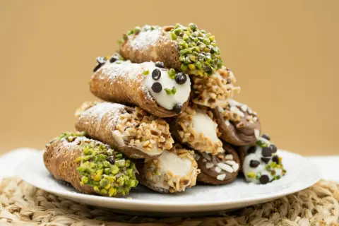 Stos idealnie udekorowanych cannoli z ricottą, posypanych cukrem pudrem, pistacjami i orzechami.