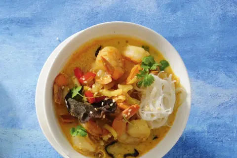 Aromatyczna zupa krewetkowa po tajsku z krewetkami, makaronem ryżowym, papryczką chili i kolendrą na niebieskim tle.