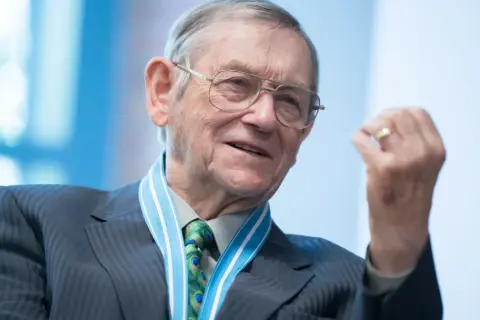 Starszy mężczyzna w okularach, z medalem na szyi i krawatem z pawimi oczkami, gestykuluje. Bo przecież nie myli się ten, co nic nie robi.