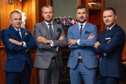 Czterech mężczyzn w garniturach stoi z założonymi rękami.
