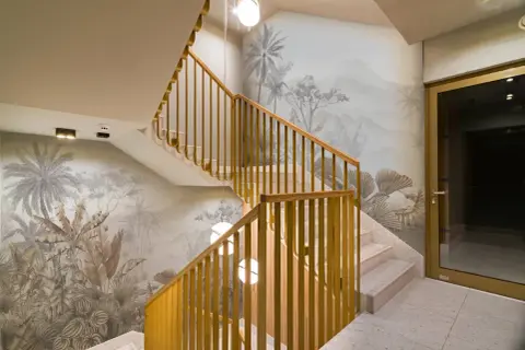 Habillage mur cage d'escalier avec un décor tropical en camaïeu. Escalier en marbre et rambarde en bois doré.