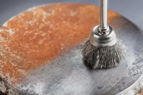 Cepillo metálico eliminando óxido de una superficie. Demuestra cómo quitar el óxido del metal, dejando una zona limpia y brillante.