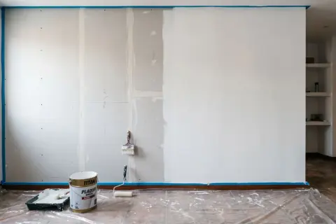 Pintar pladur es el objetivo. Cubo de pintura blanca, rodillo y brocha listos para transformar la pared.