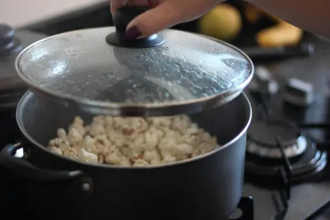 Ręka podnosi pokrywkę garnka, spod której widać gotowy popcorn. Tak właśnie robi się popcorn w garnku!