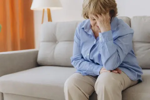 Femme âgée assise sur un canapé, la main sur le front, évoquant la recherche d'un hypotension traitement naturel.
