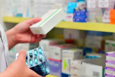Farmaceuta trzyma opakowanie leku i kilka blistrów kapsułek. Pokazuje, ile ważna jest recepta i prawidłowe dawkowanie.