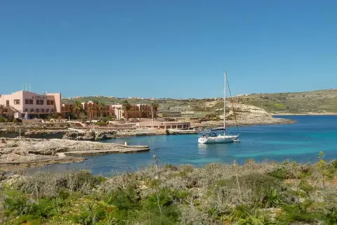 Traumhafter Urlaub auf Malta: Ein Segelboot ankert in einer Bucht vor dem Comino Hotel, umgeben von Felsen und mediterraner Vegetation.