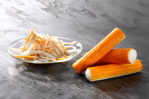 Surimi co to? Pomarańczowe paluszki i pokrojone w słupki surimi na talerzyku.