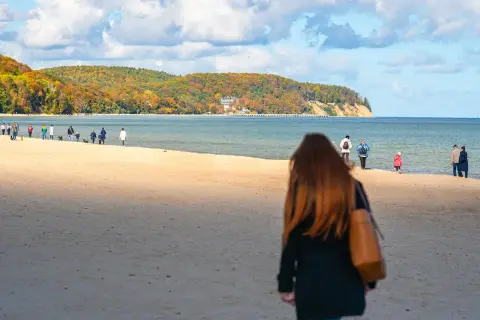 Jesień nad morzem. Spacerowicze na plaży, w oddali widać klify i las. Gdańsk Sopot odległość plażą.