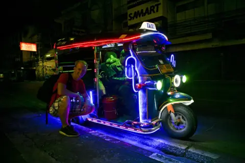 Uśmiechnięty turysta przy neonowym tuk tuk taxi w Tajlandii. Nocne światła tworzą magiczną atmosferę.