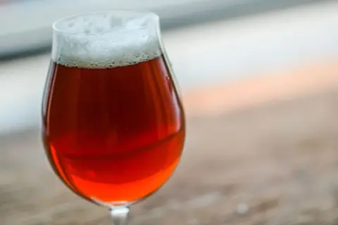 Un bicchiere di irish red ale con schiuma bianca, su un tavolo di legno.
