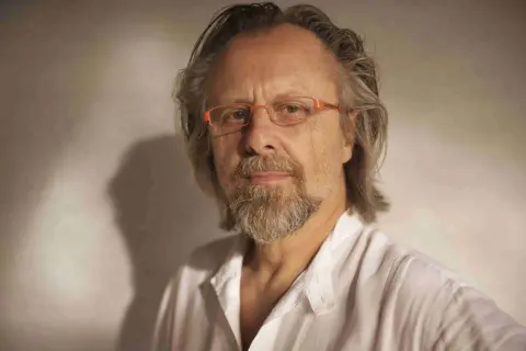 Portret mężczyzny w okularach, jednego z polskich kompozytorów współczesnych, z siwiejącą brodą i włosami, w białej koszuli.