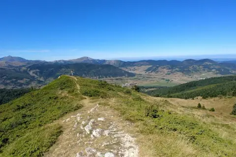 Vue panoramique depuis le col du Chioula, avec un randonneur contemplant les montagnes verdoyantes et le ciel bleu.