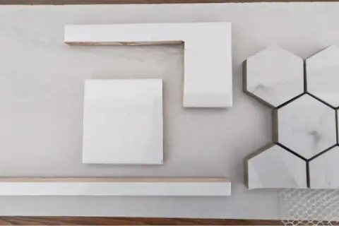 White wall tiles, including square, L-shaped, and hexagonal pieces, are laid out on a light surface, hinting at how to cut wall tile for a project.