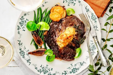 En lyxig biff med cafe de paris-smör, gröna bönor, rostade schalottenlökar och potatis. Serveras med ett glas vitt vin.
